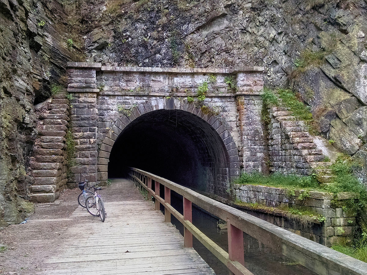 3/4 view of entrance to Paw Paw Tunnel . Stone archway with stone staircases on either side set into the face of a mountain.